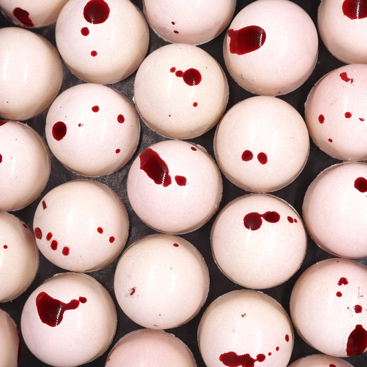 Overhead shot of array of white handmade chocolate bonbons with red drop effect